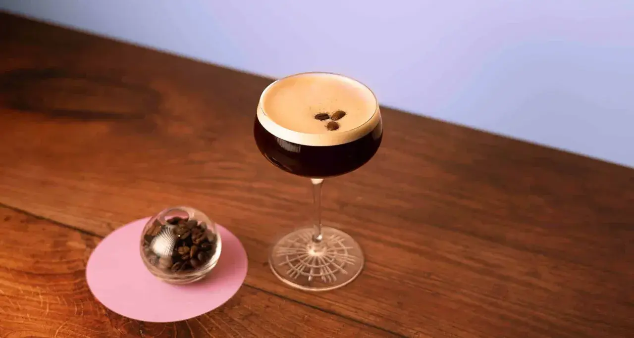 Un elegante cocktail espresso martini, con chicchi di caffè a guarnire, accanto a una piccola sfera di vetro piena di chicchi.