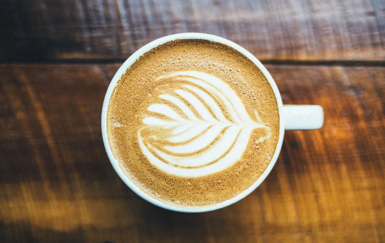 Un cappuccino con latte art su un tavolo di legno. Chissà chi ha inventato il cappuccino, ma questa tazza è perfetta.