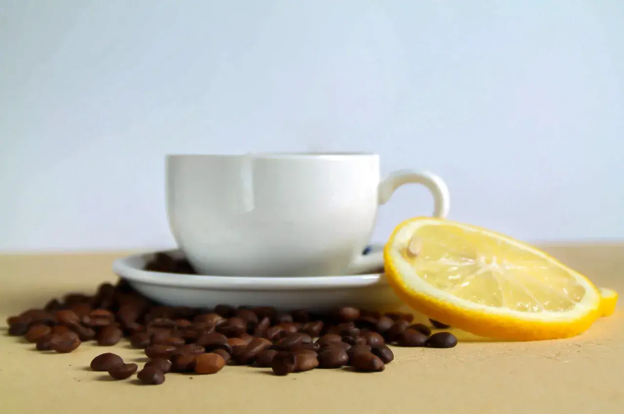 Tazzina di caffè con chicchi sparsi e una fetta di limone, un contrasto di sapori per iniziare la giornata.