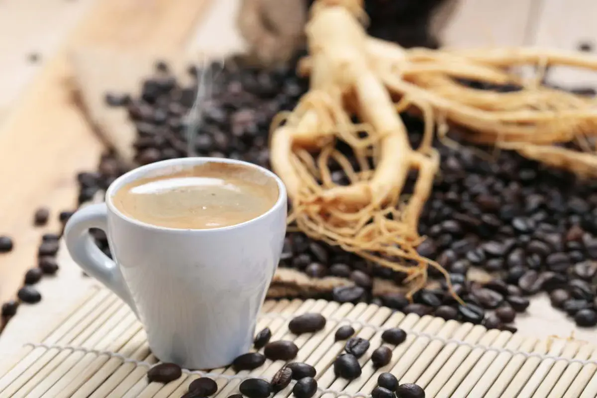 Tazza di caffè fumante accanto a chicchi tostati e radice di ginseng, che contiene caffeina per un risveglio energico.