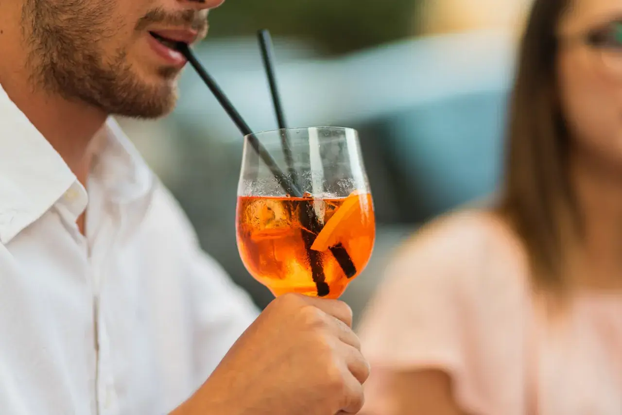 Un uomo sorseggia un Aperol Spritz, perfetto per la sua aperitivo ricetta. Ghiaccio e arancia completano il drink.