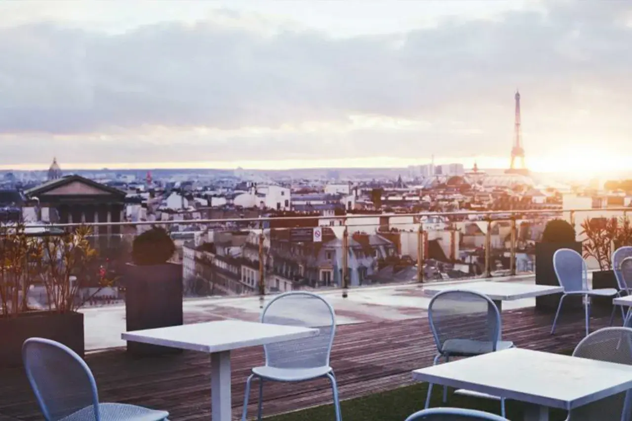 Terrazza con vista su Parigi al tramonto, tavoli e sedie vuoti, la Torre Eiffel sullo sfondo. Un luogo perfetto per godersi i locali storici di Parigi.
