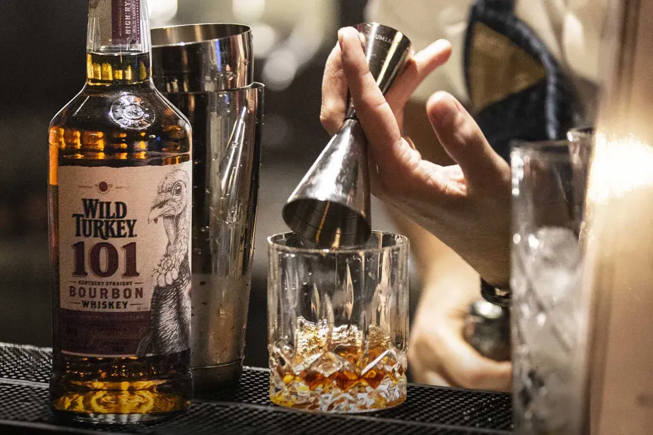 Un barista prepara un bourbon drink versando il Wild Turkey 101 in un bicchiere con ghiaccio.