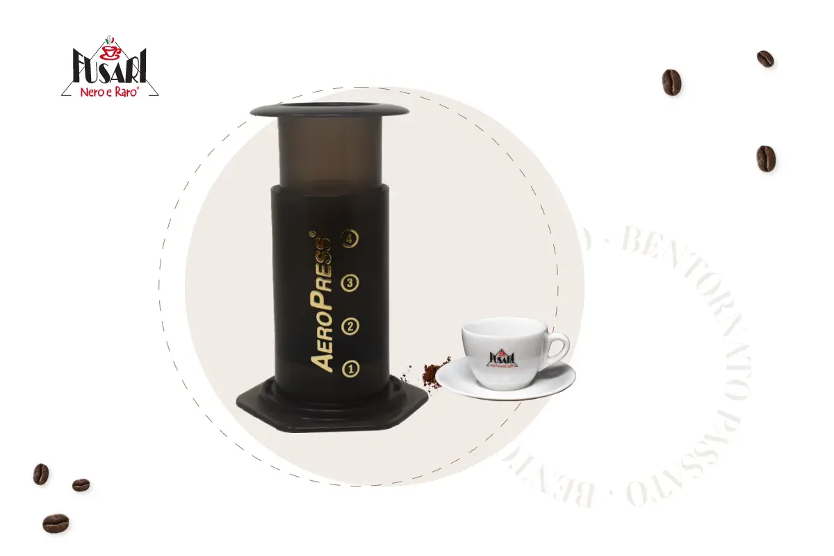 AeroPress per un caffè perfetto. Accanto, una tazzina bianca con logo e chicchi di caffè sparsi.