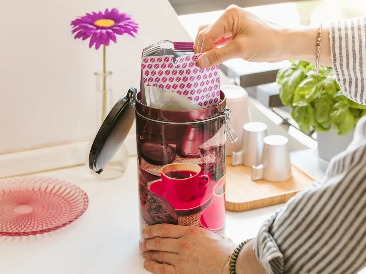 Mano inserisce pacchetto di caffè in una lattina decorata con chicchi e tazzina. Si può congelare il caffè liquido per conservarlo al meglio.