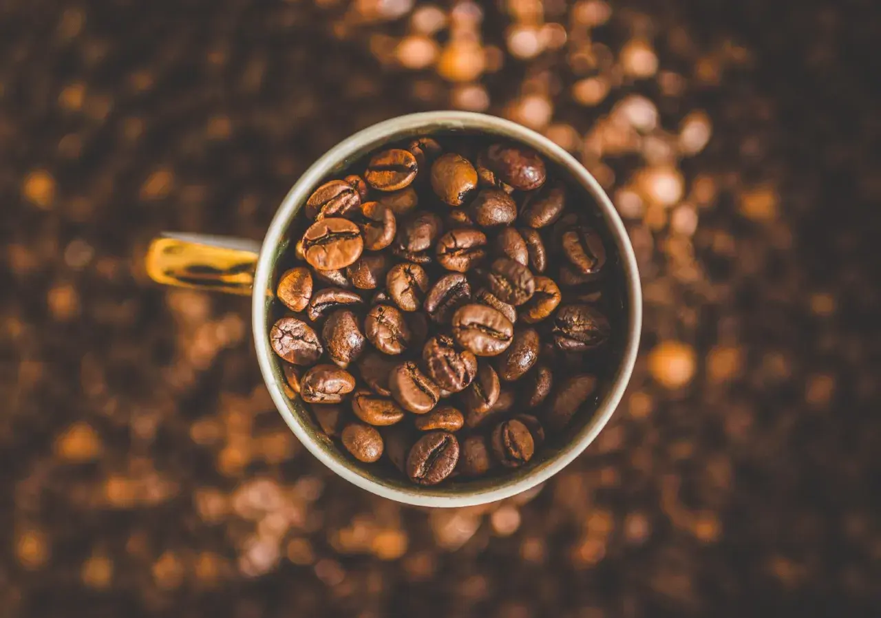 Tazza piena di chicchi di caffè tostati, un invito a gustare la bevanda che fa passare la fame.