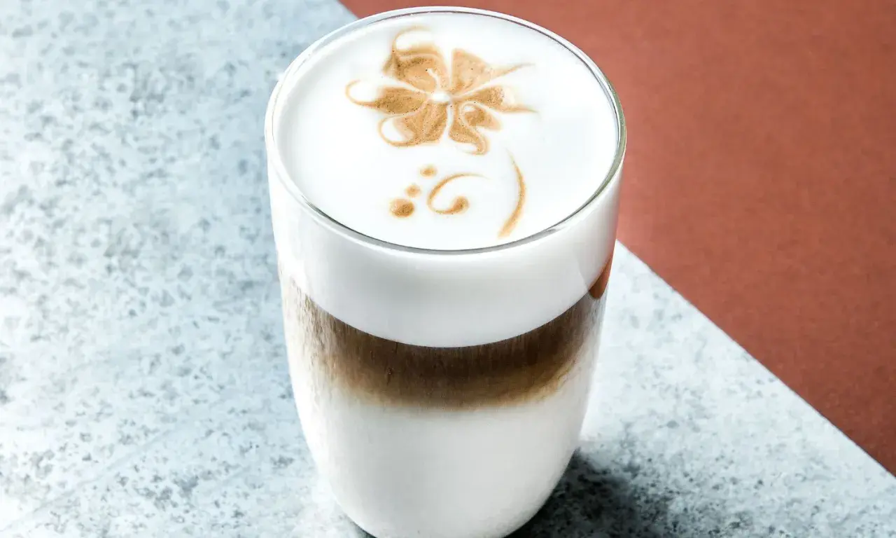 Un delizioso cappuccino freddo con schiuma decorata a forma di fiore, servito in un bicchiere trasparente.