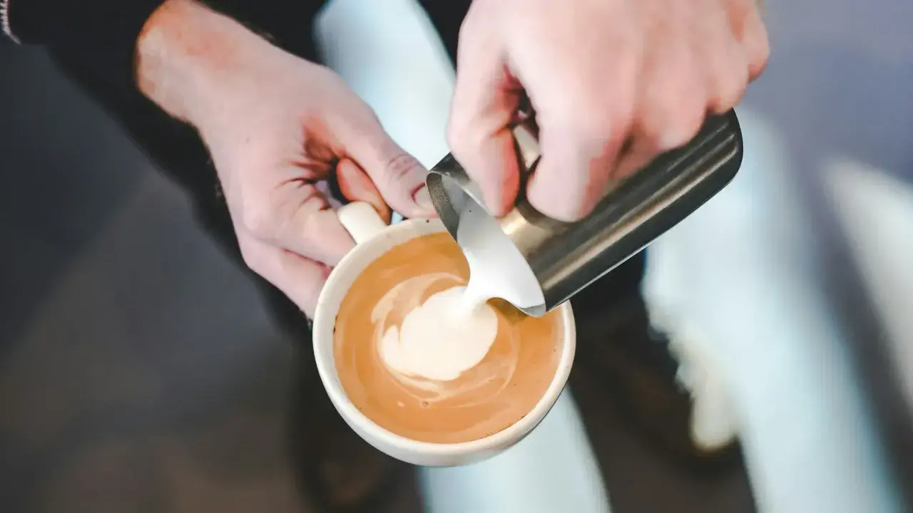 Mani esperte versano latte per cappuccino, creando un disegno sulla schiuma.