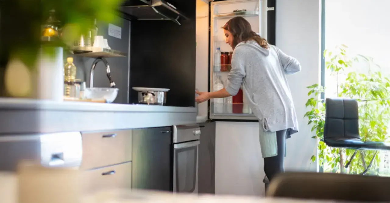 Donna prende una bottiglia dal frigo. Forse cerca il caffè in frigo per preparare una bevanda rinfrescante.