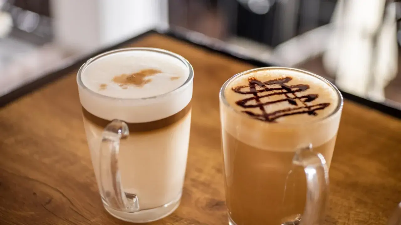 Due caffè in tazza: un macchiato vs latte con schiuma e decorazione al cioccolato.