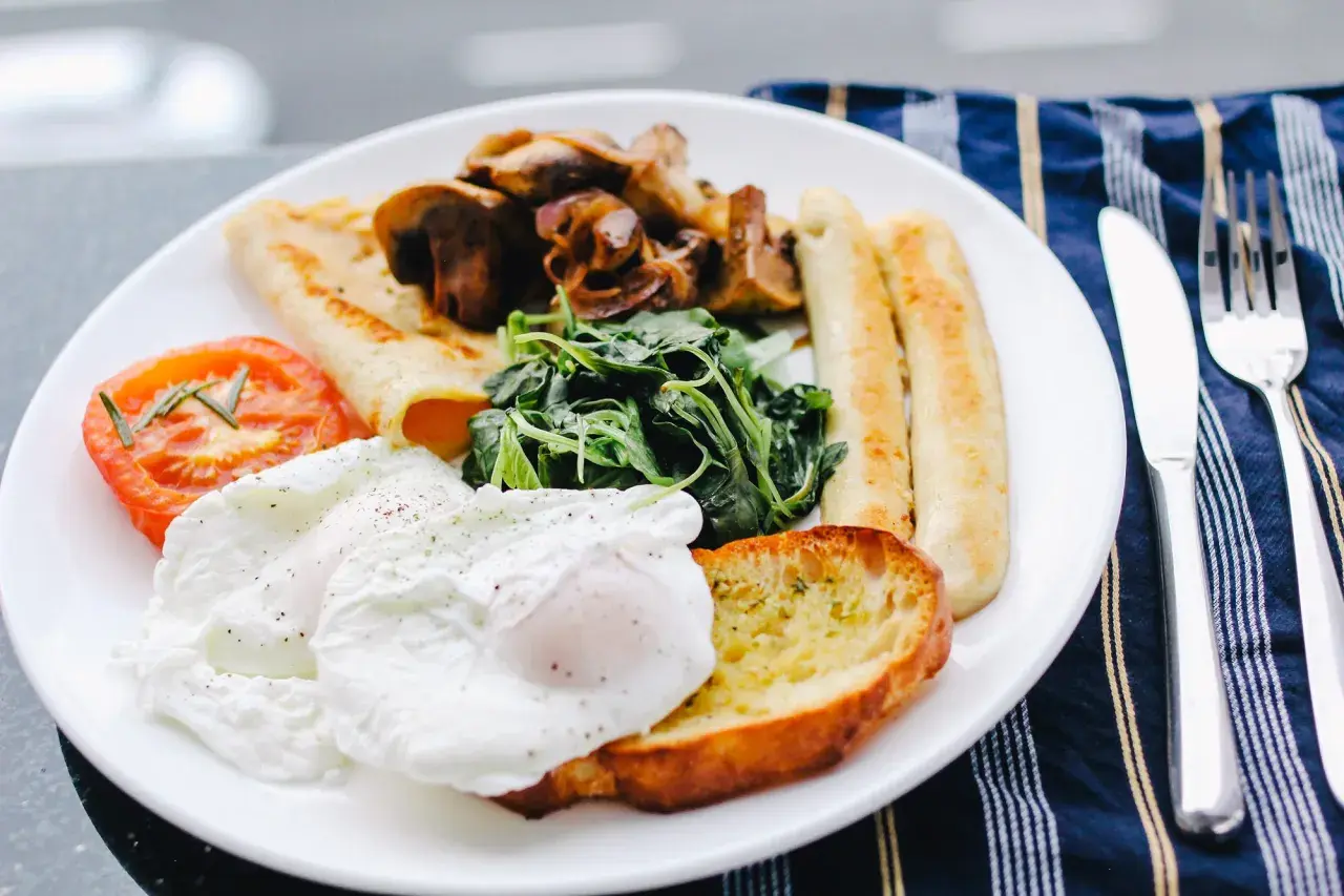 Un piatto ricco per una colazione continentale: uova in camicia, pomodoro, funghi, spinaci, pane tostato e salsicce.