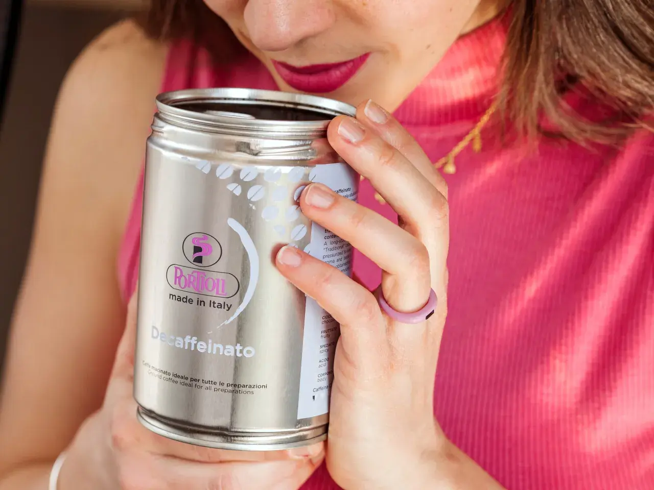 Donna annusa una lattina di caffè decaffeinato, godendosi l'aroma. Un caffè con meno caffeina, perfetto per ogni momento.