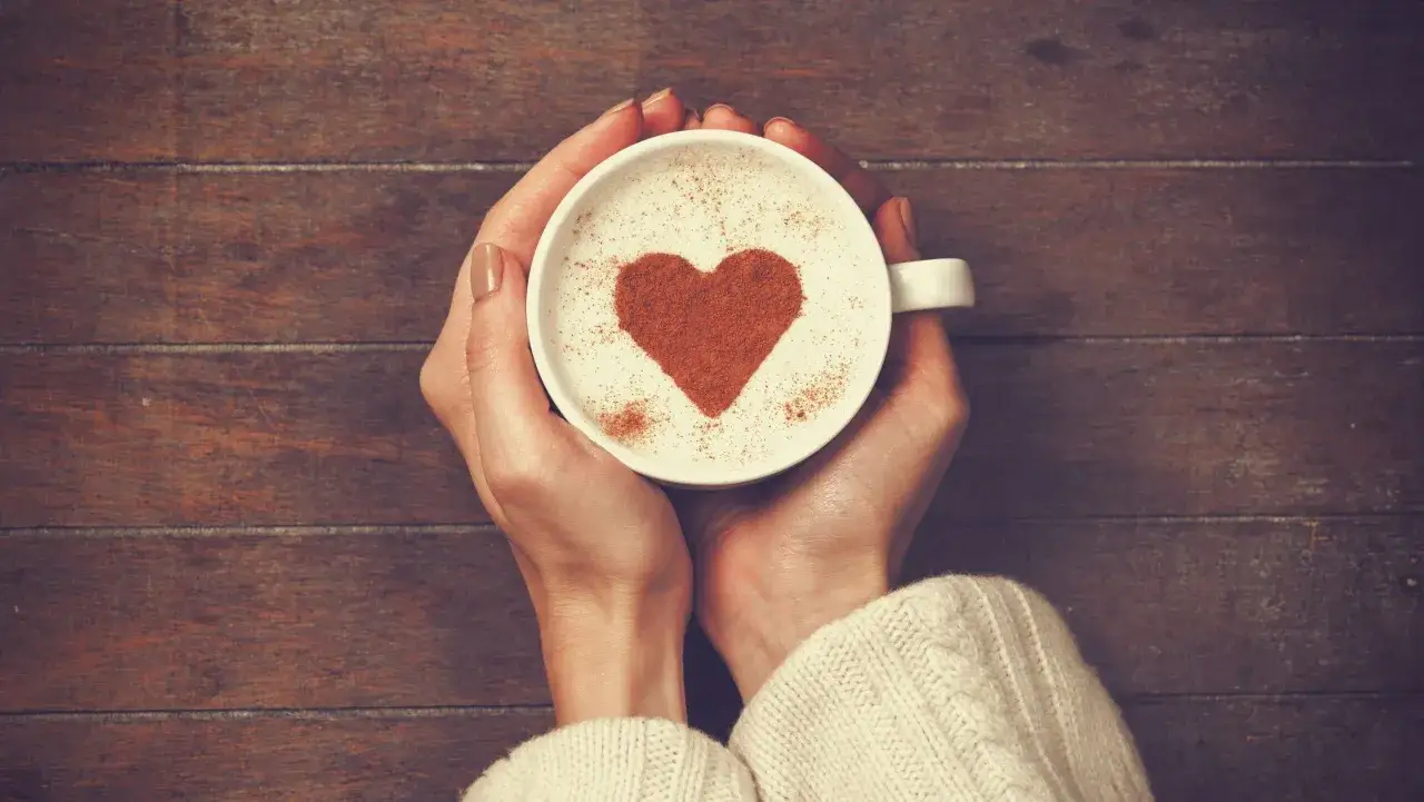 Mani che stringono una tazza di caff&egrave; con un cuore di cannella, perfetto per San Valentino.