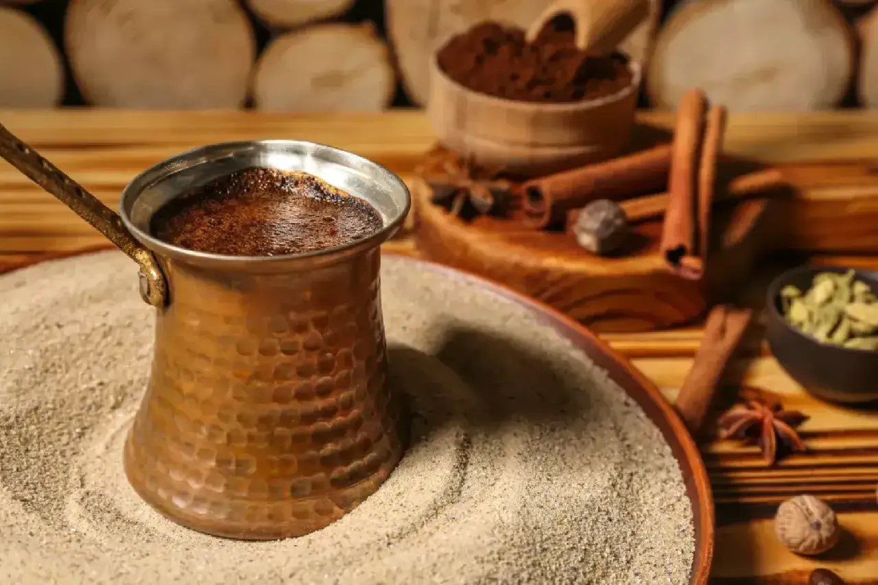 Caff&egrave; turco fumante nella cezve, pronto per essere gustato. Impara come usare la turca per un'esperienza autentica. Spezie e caff&egrave; macinato completano la scena.