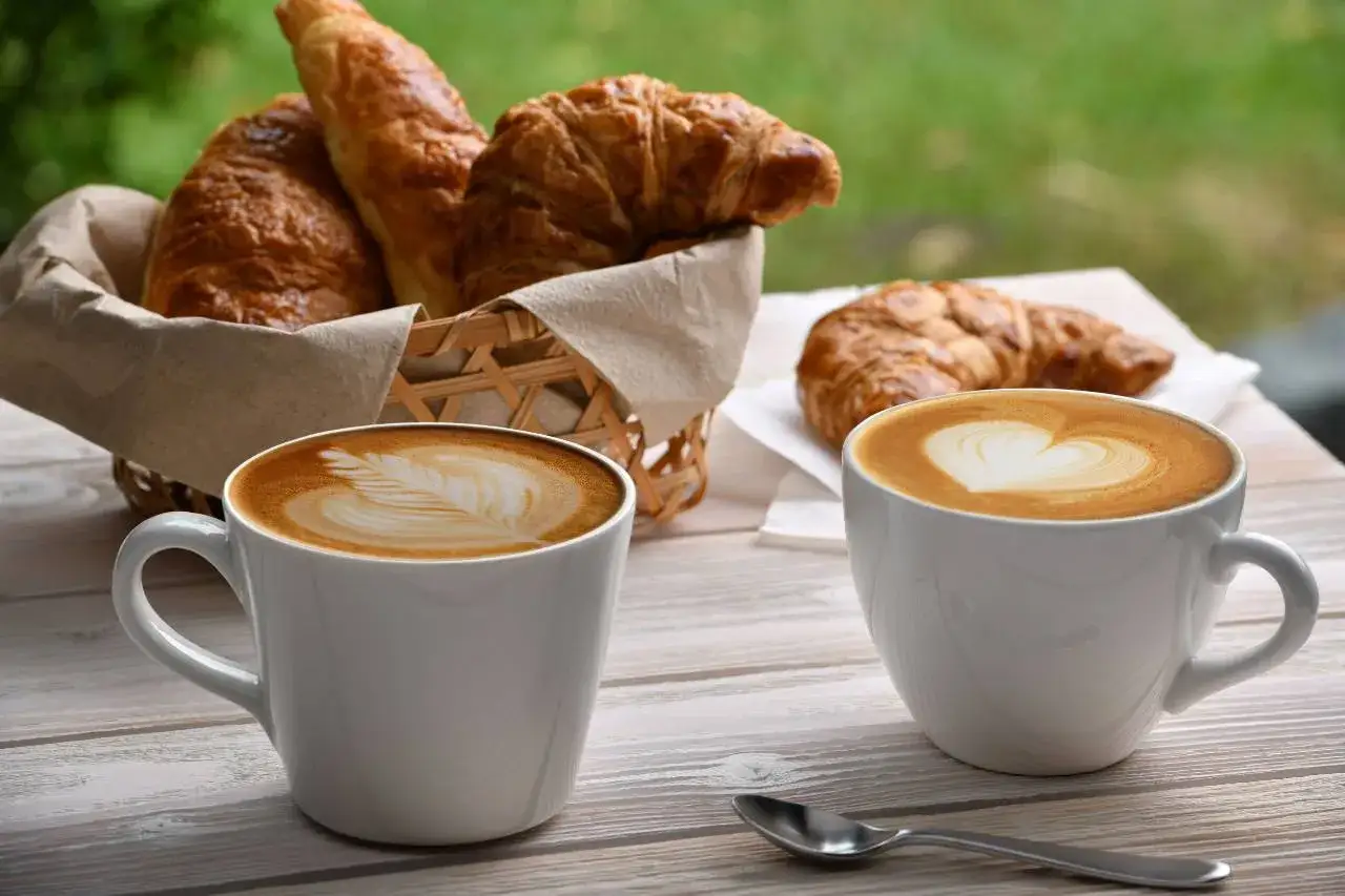 Due tazze di cappuccino con latte art e croissant in un cestino, perfette bevande per colazione.