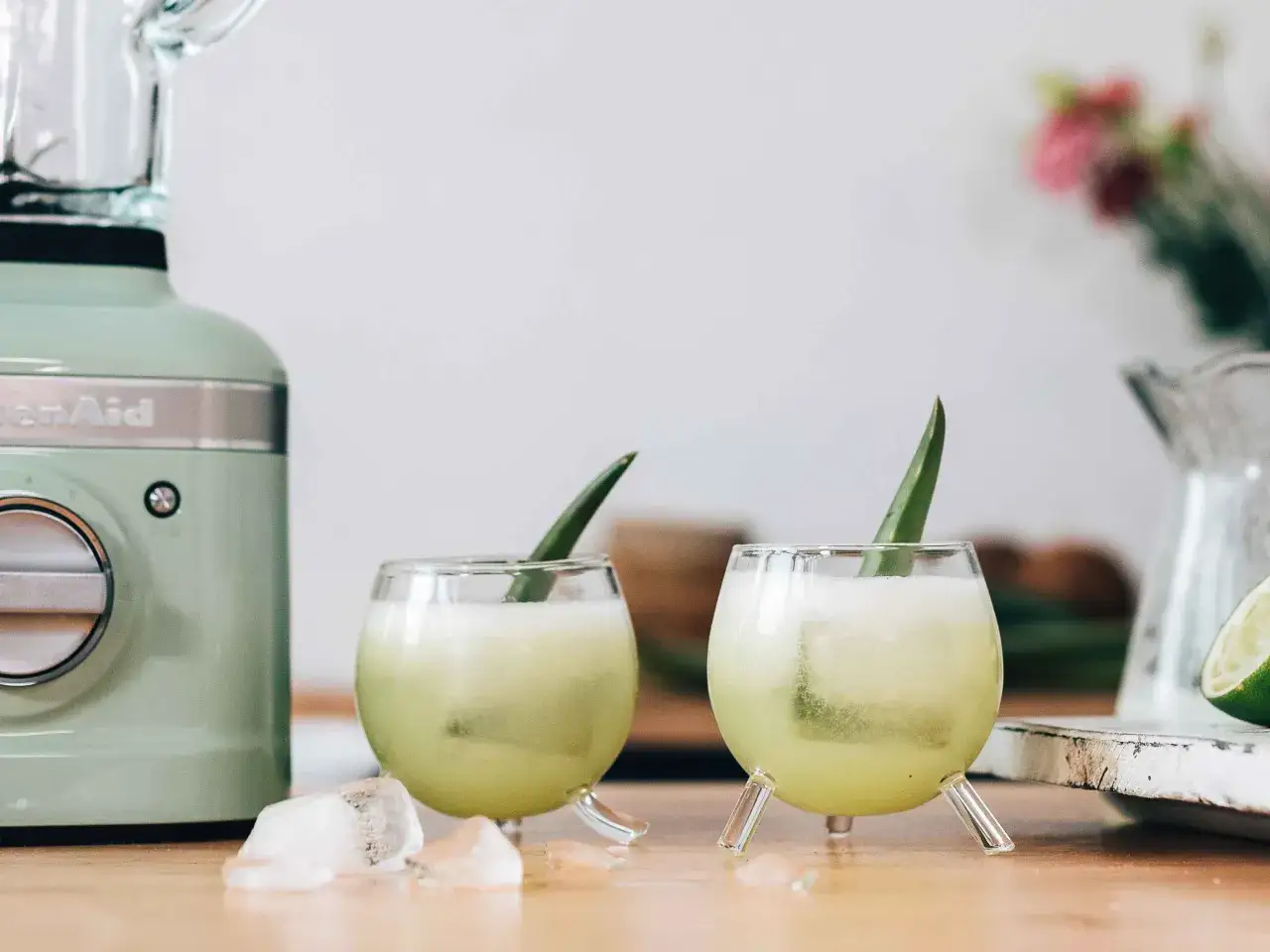 Due bicchieri di analcolico dolce, rinfrescante e cremoso, con foglia di aloe e ghiaccio. Mixer verde sullo sfondo.