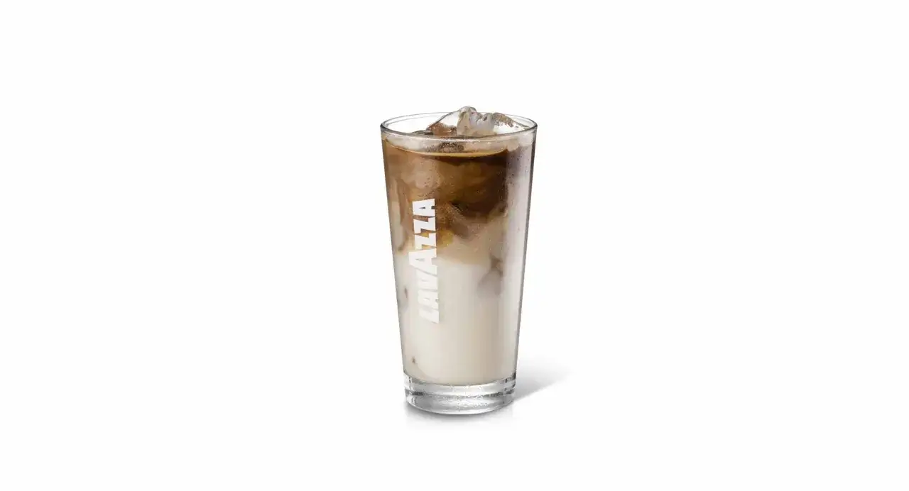 Un bicchiere alto di iced coffee latte Lavazza con cubetti di ghiaccio e striature di caffè e latte.