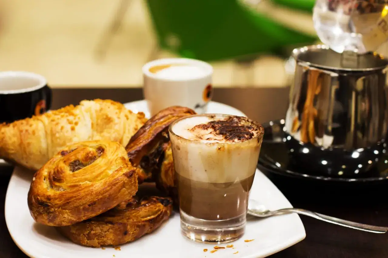 Un delizioso cappuccino, croissant e dolci da forno su un piatto bianco.