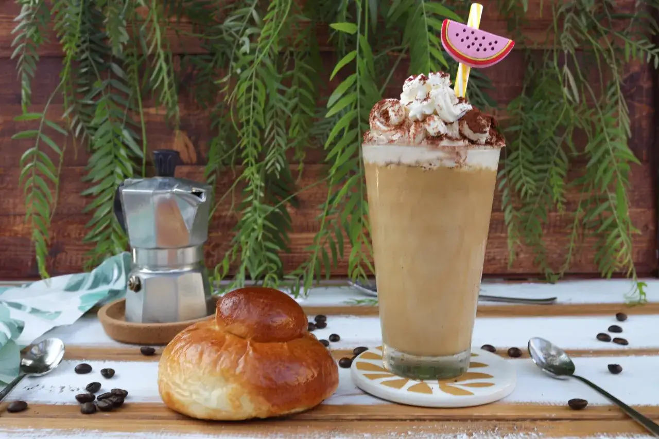 Un delizioso frappe al caff&egrave; con panna e cacao, accompagnato da un brioche e una moka.
