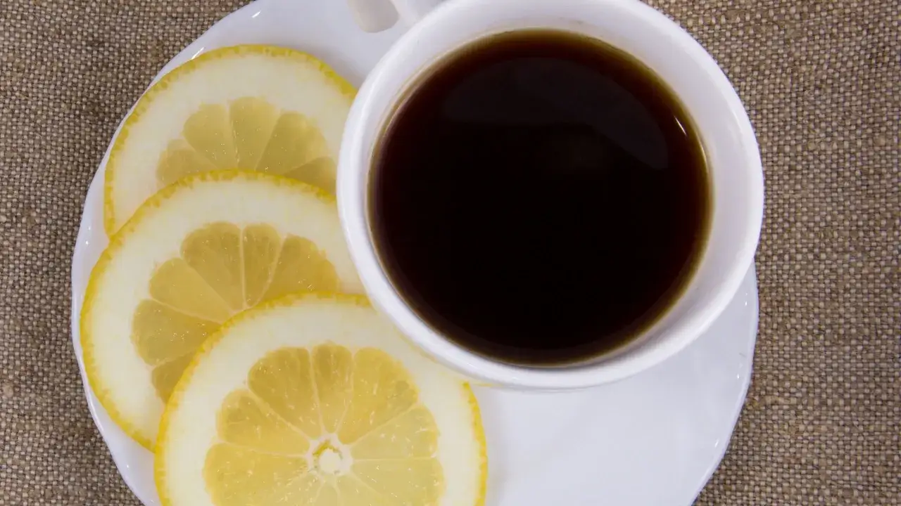Tazza di caffè nero con fette di limone su un piattino bianco, un'idea per una colazione energizzante.