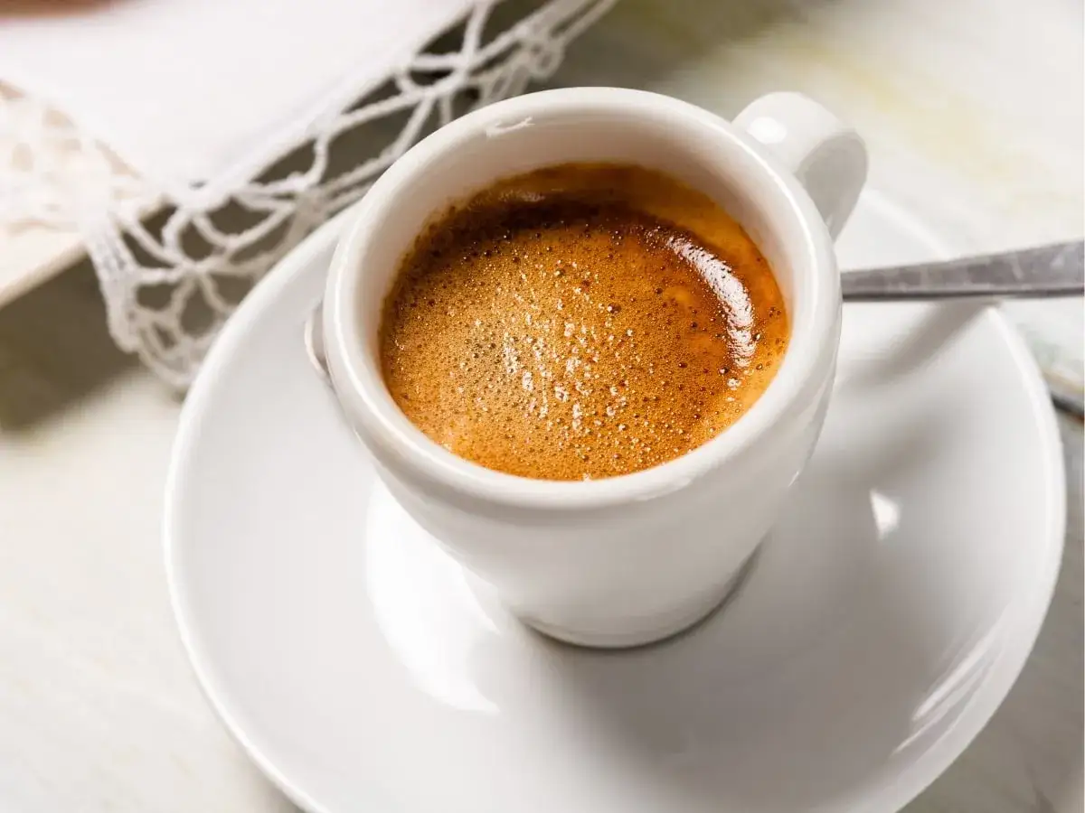 Un invitante caff&egrave; liscio con una crema dorata, servito in una tazzina bianca su un piattino. Un momento di puro piacere.