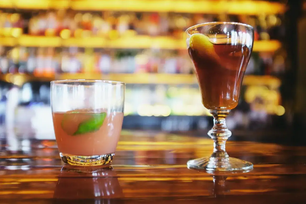 Due cocktail su un bancone di legno lucido, uno con una fetta di lime e l'altro con una guarnizione verde. Un classico bourbon drink pronto da gustare.