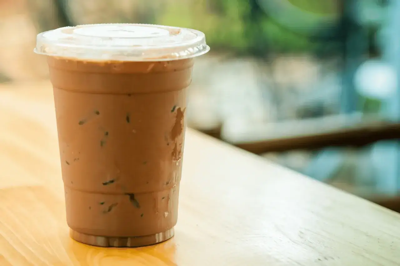 Un bicchiere di caffè decaffeinato freddo, perfetto per i bambini, con ghiaccio e una cannuccia, su un tavolo di legno.