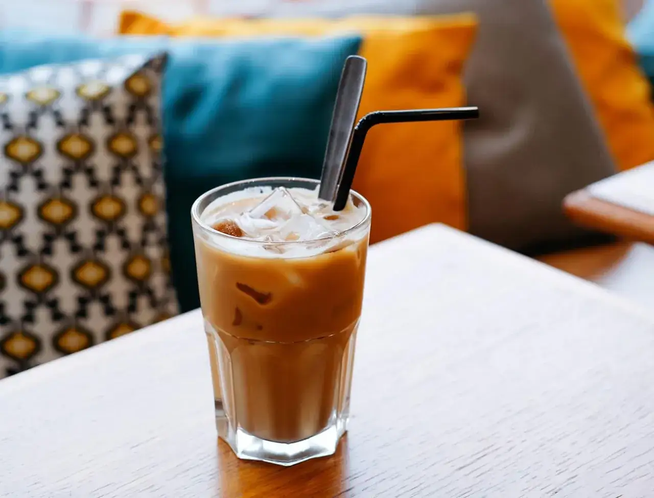 Un rinfrescante caffè freddo al bar, con ghiaccio e cannuccia nera, su un tavolo di legno.