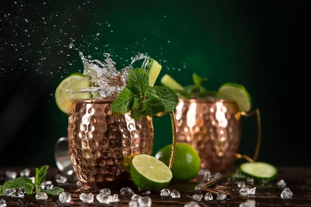Moscow Mule: lime, menta e zenzero, ingredienti freschi per un drink rinfrescante. Ghiaccio e schizzi d'acqua completano la scena.