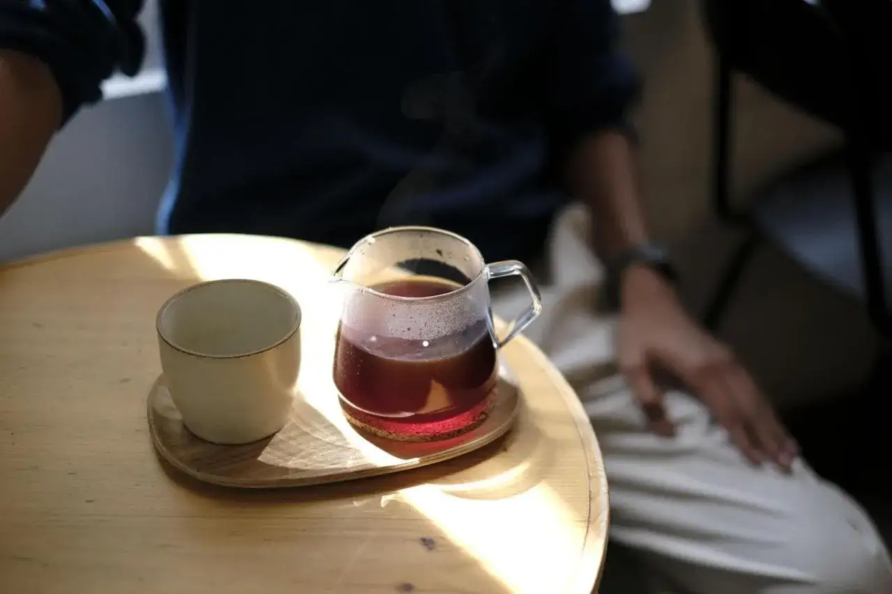 Un bicchiere di vetro con caffè speciali fumante e una tazzina vuota su un tavolino di legno.