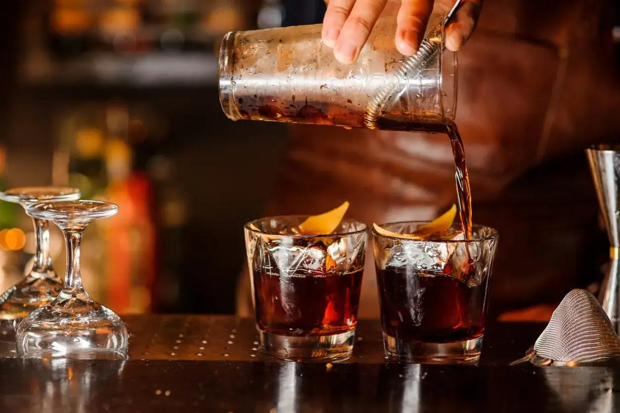 Un barista versa un bitter cocktail in due bicchieri con ghiaccio e scorza d'arancia.
