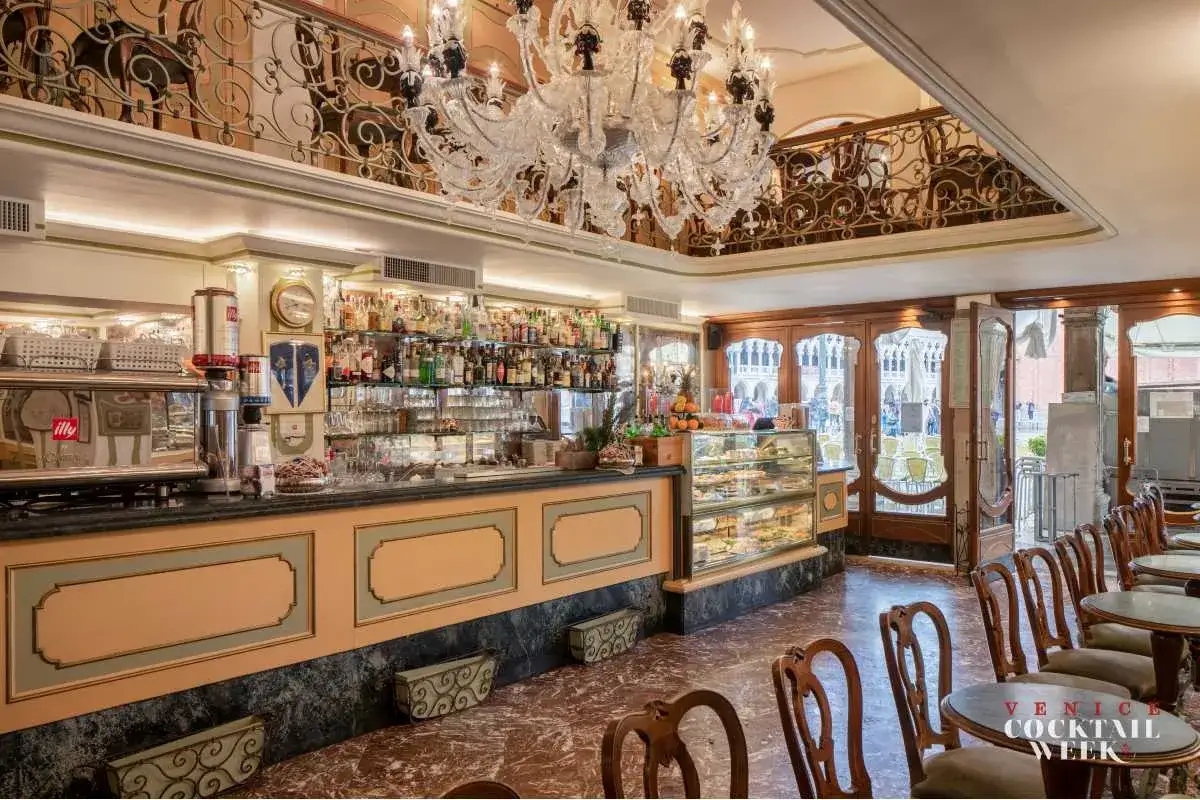Interno di un caff&egrave; storico a Venezia, con bancone bar, vetrine di dolci e un lampadario di cristallo.
