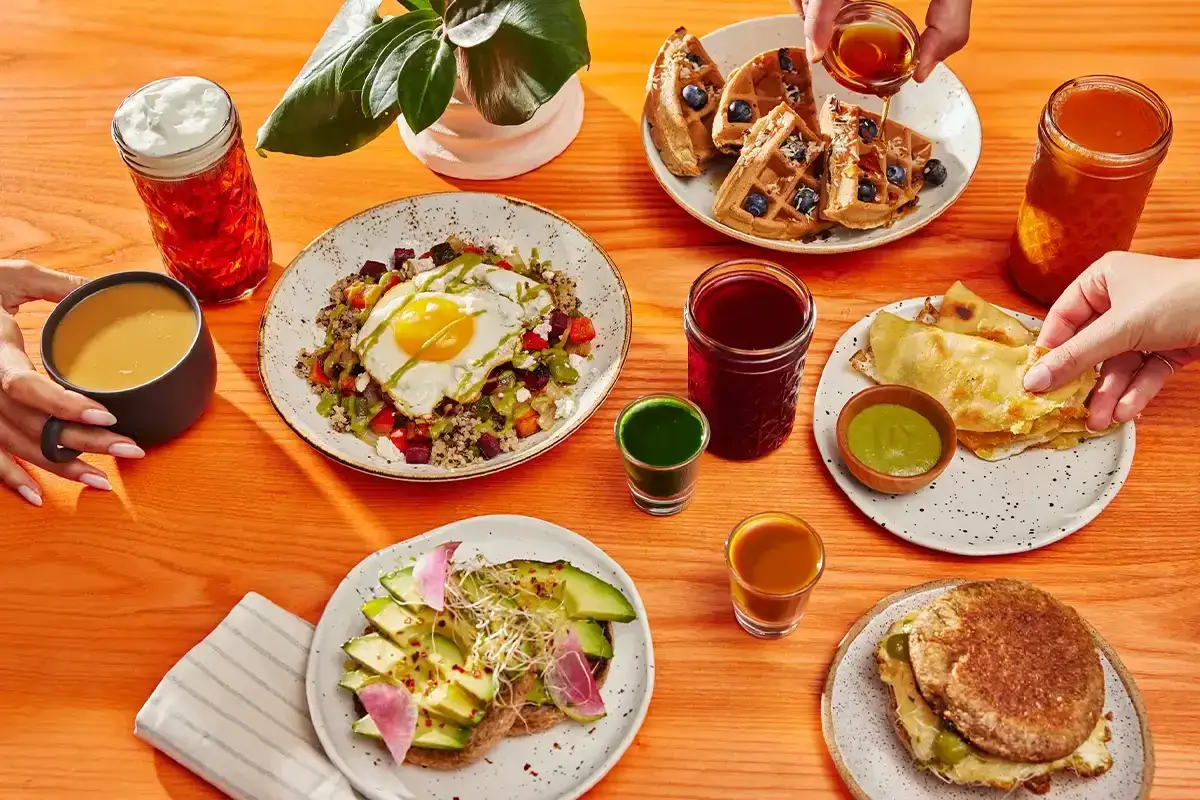 Varietà di piatti sani: toast avocado, quinoa con uovo, waffle, hamburger e succhi. Ideale per capire cosa prendere al bar a dieta.