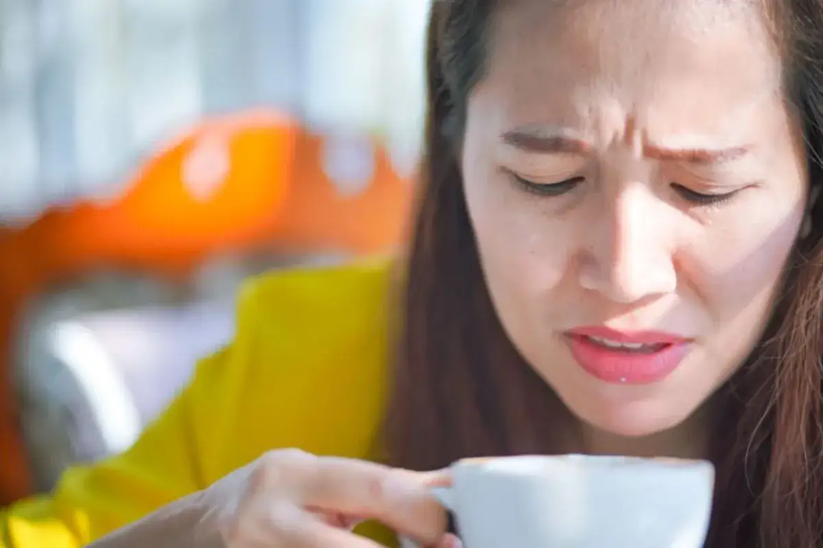 Donna con espressione corrucciata assaggia una tazza di caff&egrave;, forse perch&eacute; il caff&egrave; &egrave; astringente.