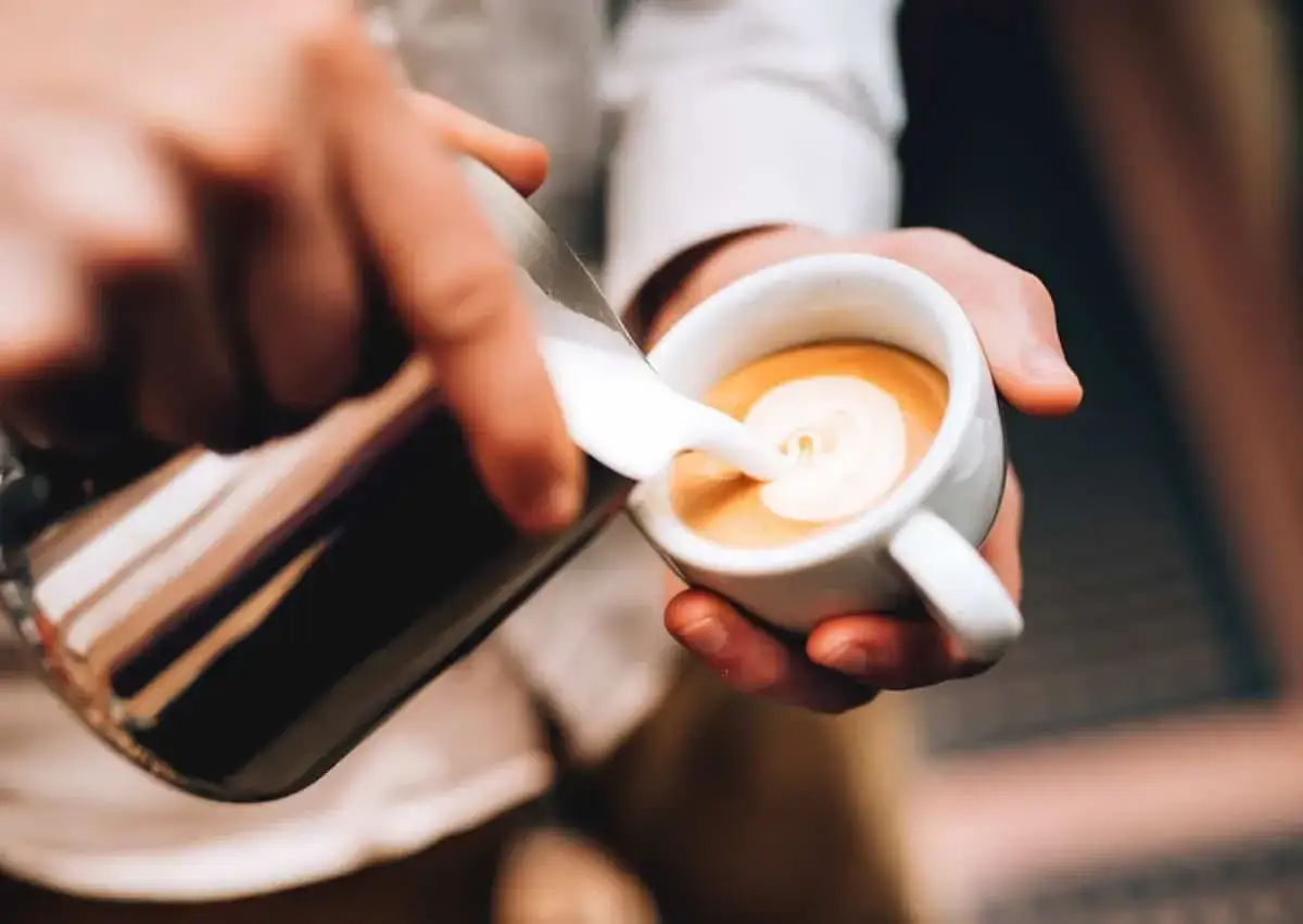 Un barista prepara un doppio macchiato, versando la schiuma di latte in una tazzina di caff&egrave;.
