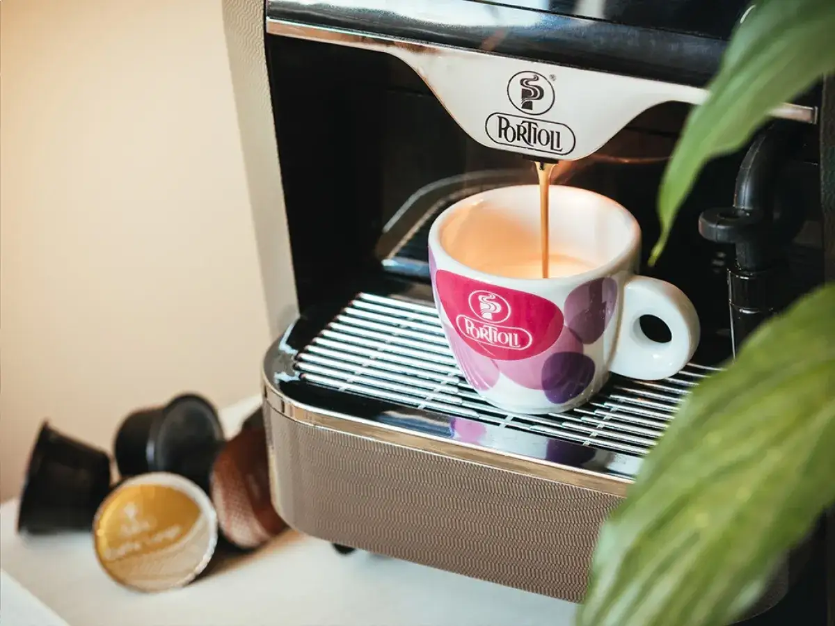 Macinatura caff&egrave; bar: una tazzina colorata raccoglie un espresso fumante da una macchina moderna. Capsule di caff&egrave; sparse.
