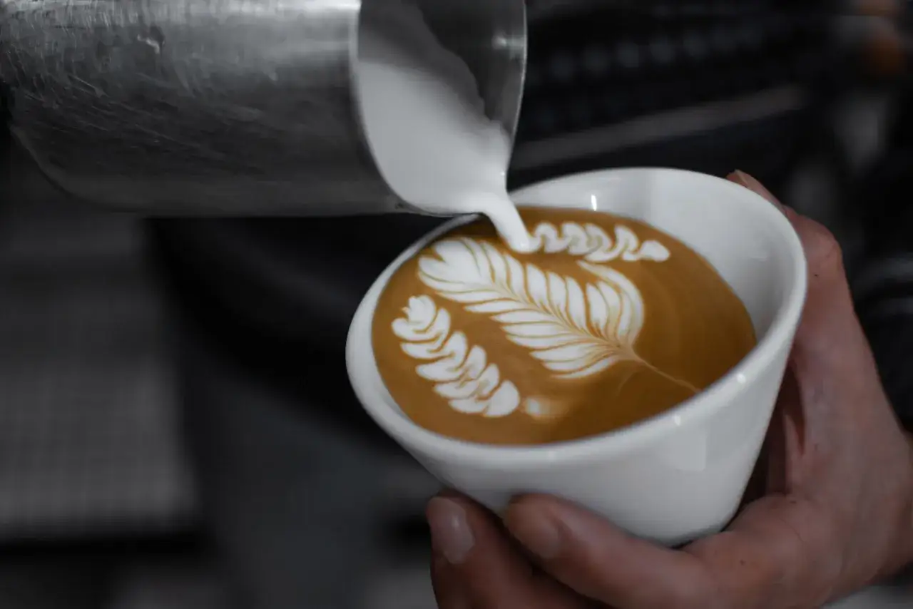 Un barista crea un'arte del caff&egrave; con schiuma di latte, un design a foglia su un cappuccino.