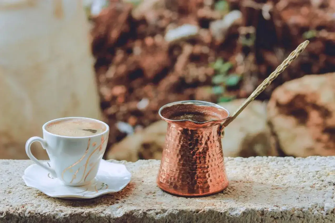 Caffè turco pronto in tazza, accanto al bricco di rame. Scopri come fare il caffè turco senza cezve per un'esperienza autentica.