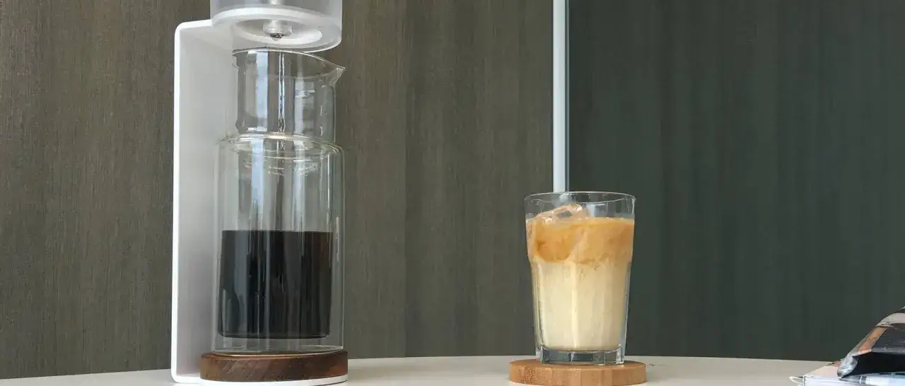 Un bicchiere di cold brew latte con ghiaccio, accanto a un infusore per caff&egrave;.