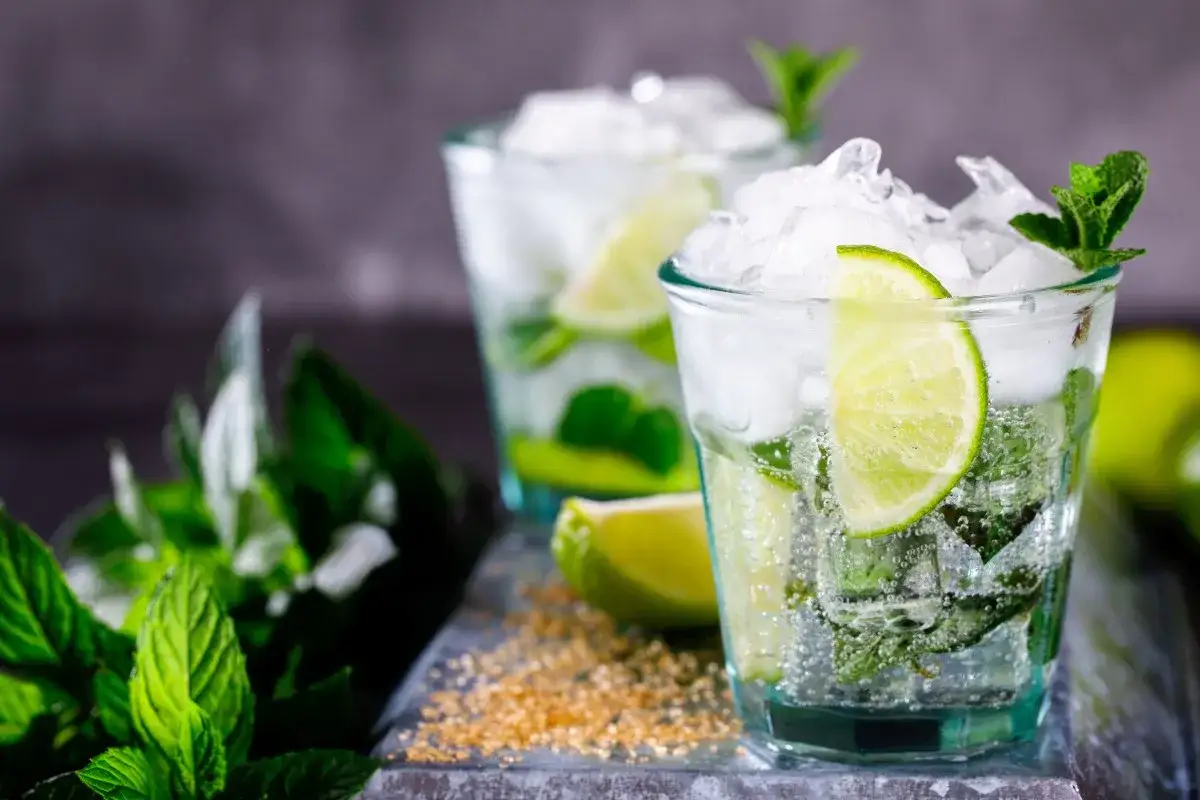 Due bicchieri di mojito, con menta fresca, lime e ghiaccio tritato. La ricetta perfetta per un'estate rinfrescante.