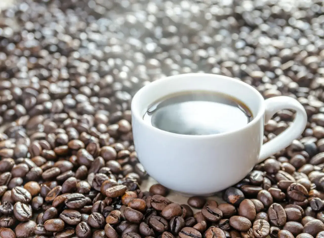 Tazza di caff&egrave; fumante su un letto di chicchi tostati. Quanti caff&egrave; al giorno ti servono per iniziare la giornata?