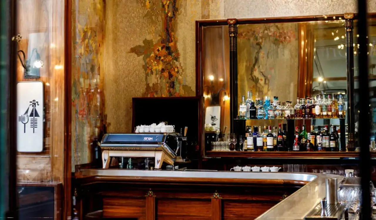 Un elegante caff&egrave; illuminismo con un bancone in legno scuro, una macchina per caff&egrave; e bottiglie di liquore su uno scaffale riflettente.