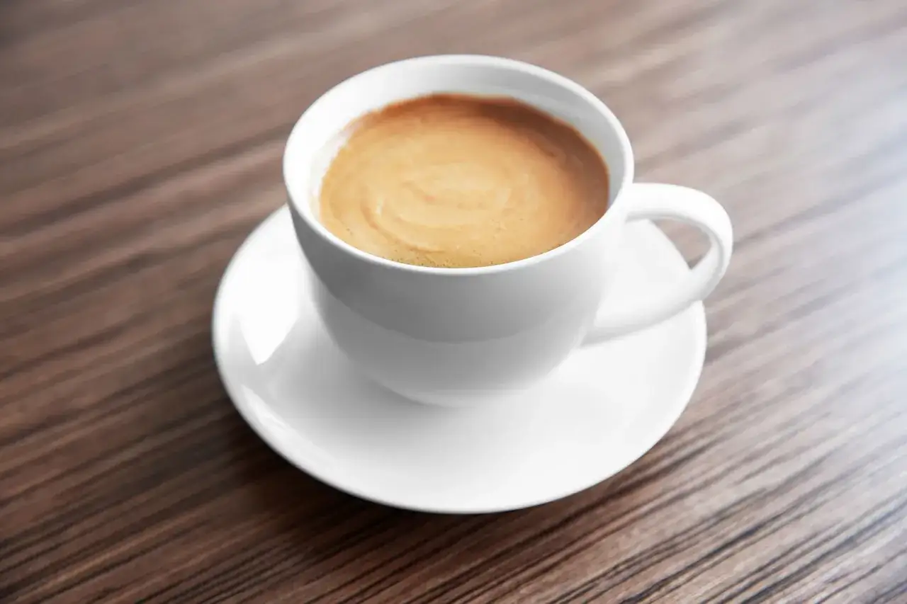 Tazza bianca con caff&egrave; e schiuma su piattino, ideale per chi cerca un'opzione a basso contenuto di calorie ginseng.