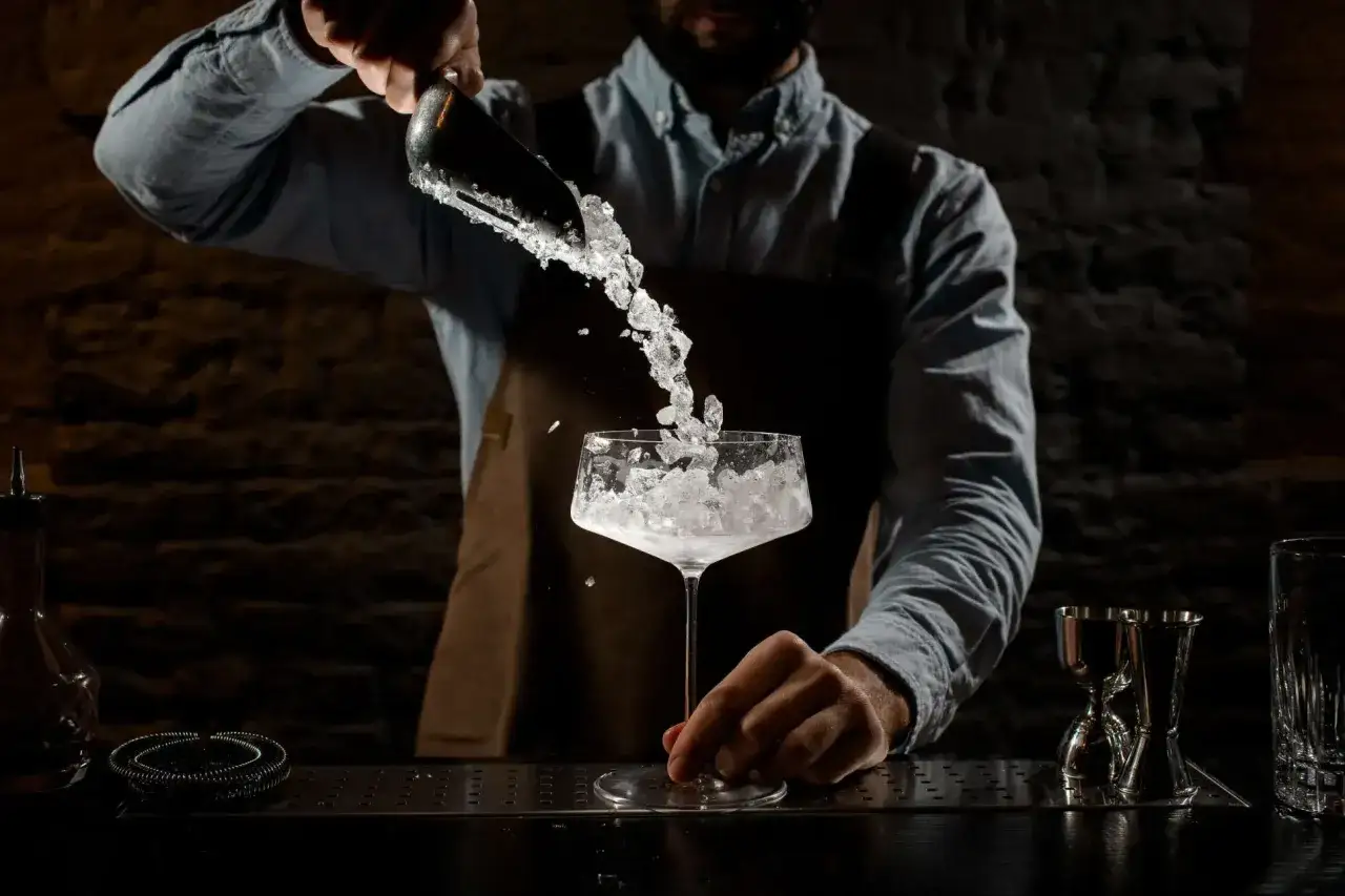 Barman aggiunge ghiaccio tritato a un bicchiere, creando un cocktail rinfrescante.