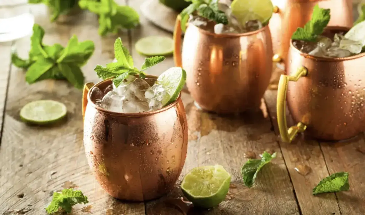 Moscow mule drink in ramekin di rame, con ghiaccio, lime e menta su un tavolo di legno.