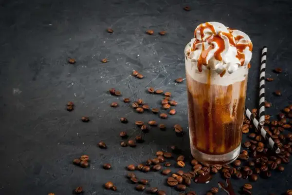 Un delizioso frappe al caffè con panna montata e sciroppo al caramello, circondato da chicchi di caffè tostati su sfondo scuro.