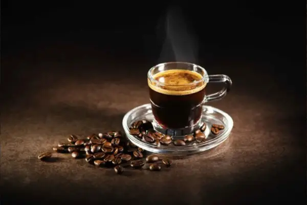 Un fumante caffè al vetro, con chicchi tostati sparsi attorno, evoca un momento di puro piacere.